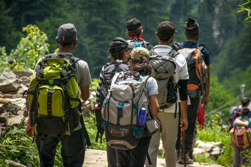 A group of students in a single file, carrying backpacks, heading into the forest in what looks like venturing into a field studies adventure