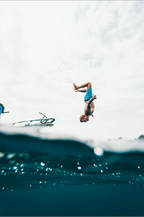 Picture of a man in blue shorts, head facing mid-air about to dive in water, possibly while on an adventure studying abroad