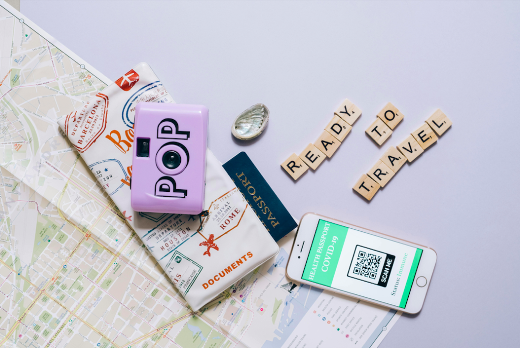 A picture of a passport, a map, a virtual vaccine certificate, and the scrabble words "ready to travel" laid out on a table.