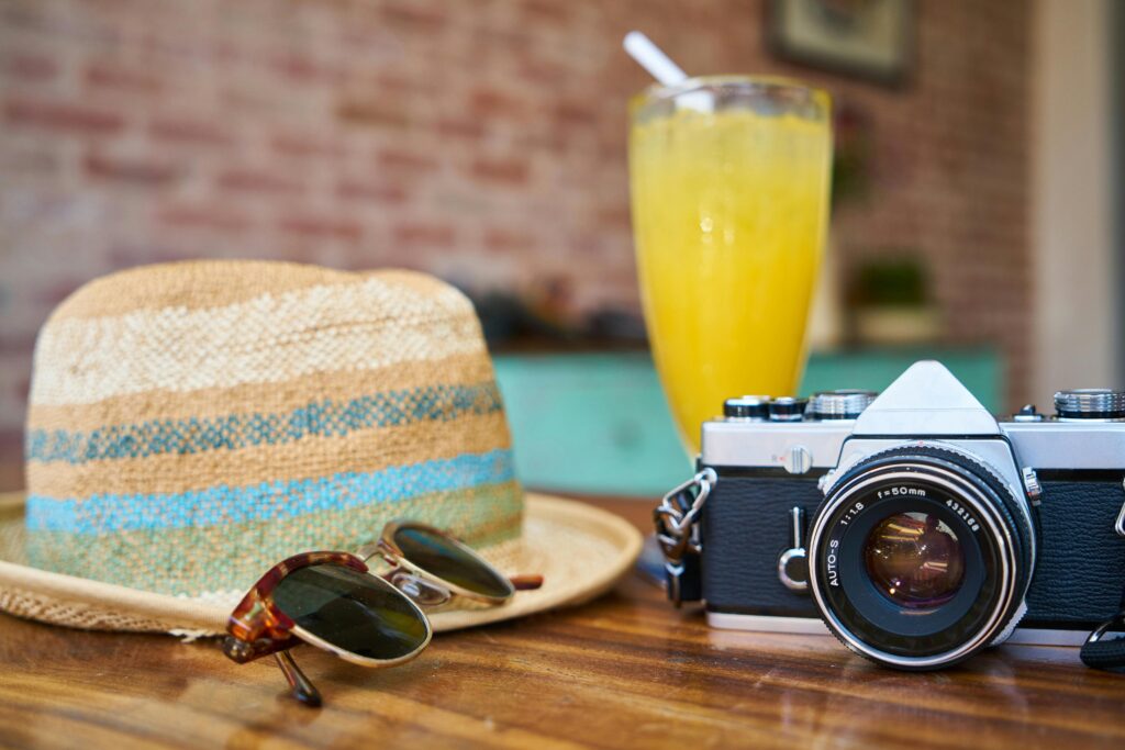 A picture of a yellow hat, a glass of juice, a camera and sunglasses, part of the things you should have when preparing for your trip